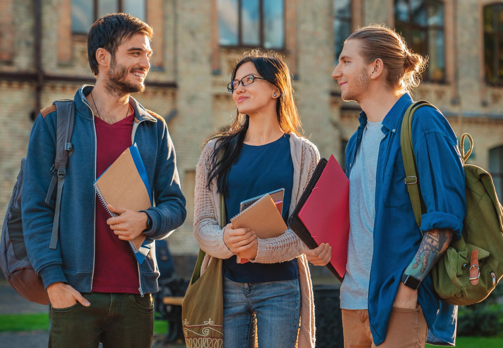3 students walking on campus holding books smiling
